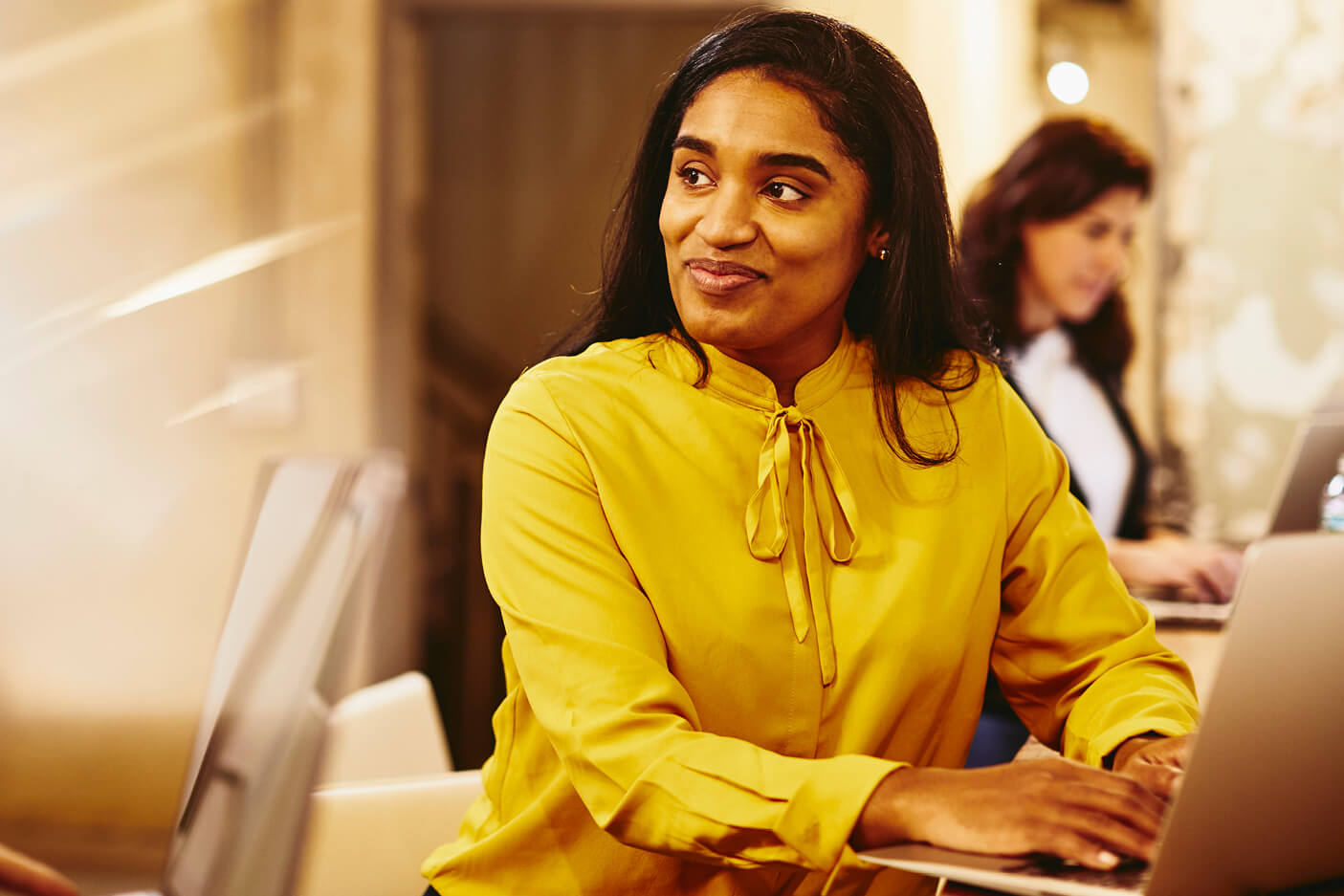 Two smiling women working on their laptop.