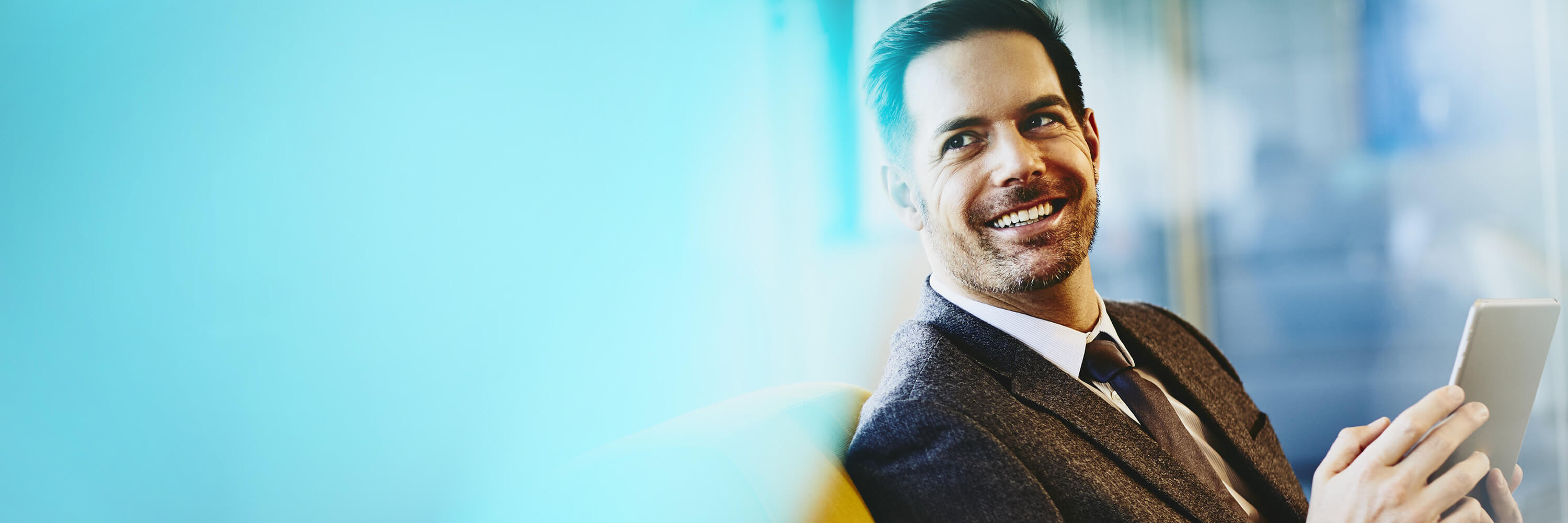 Smiling man in a suit sitting on a couch working on his tablet. 