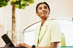 Smiling woman sitting at table working on a tablet.