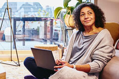 Woman leaning against a couch, sitting on the floor, with laptop on her lap