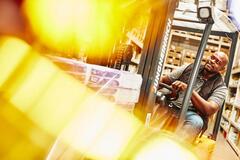 Man smiling driving a warehouse forklift and moving boxes.