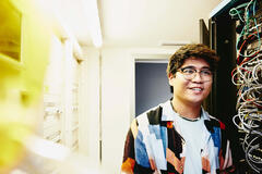 Smiling man holding a laptop standing in a servers room.