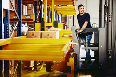 Smiling man standing on a forklift.