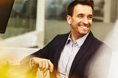 Smiling man in an office holding his glasses while sitting at his desk.