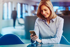 Woman in a blue shirt looking at her phone, sitting in an office. Primary color: blue.