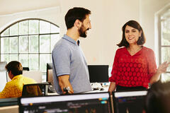 Two colleagues man and woman having a chat standing between desks.