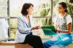 Two woman sitting on a window sill looking at papers.