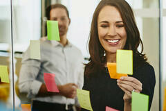 Two business women and a man in an office putting sticky notes on a window.