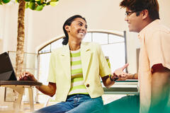 Man and woman sitting at table having a chat, while woman working on a tablet.
