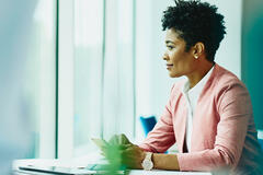 Woman sitting at a table with phone in hand. Tablet and notebook on table. Woman looking out of the window.