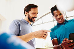 Two smiling colleagues (men) looking at a phone.