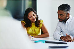 Man and woman sitting down, both looking at paperwork.