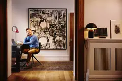 Male in a blue shirt sitting at a desk looking up, view from another room