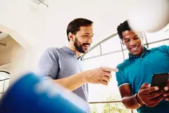 Two smiling colleagues (men) looking at a phone.
