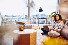 Womale leaning against a couch, sitting on the floor, with laptop on her lap
