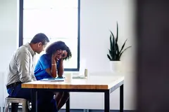 Smiling male and female sitting at a table. Both looking down at the table.