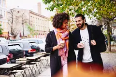 Smiling male and female having a conversation while holding drinks and walking outside.
