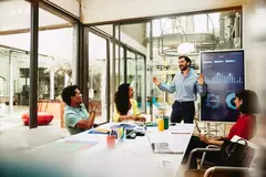 Four colleagues having a meeting in a meeting room. Financial charts in the background.
