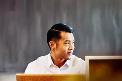 male sitting in an office, smiling and looking away.
