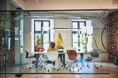 Female and male are sitting and female is standing at a table in a office meeting room