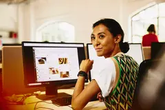 Womale sitting at her desk, looking away from computer screens displaying marketing content.
