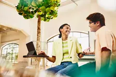male and female sitting at table having a chat, while female working on a tablet.
