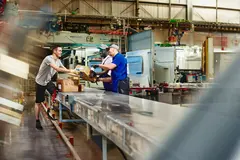 Three people working next to an assembly line with packages. 
