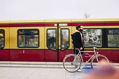 male standing on a train platform with his bike. Train in the background.
