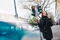 male walking outside holding his phone with earphones in.
