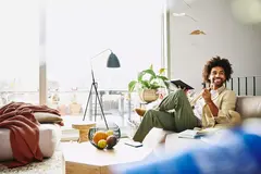 Smiling male sitting on a couch holding a notebook and a pen.
