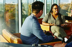 Two people having a conversation while sitting down in a lounge environment.