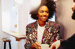 Smiling woman sitting at a table with coffee, smiling at someone.