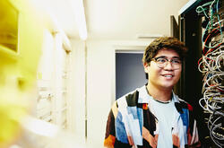 Smiling man holding a laptop standing in a servers room.
