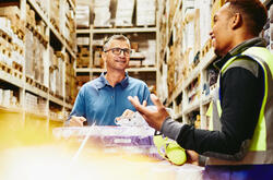 Two man in a warehouse alley with a trolley full of packages.