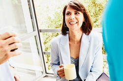 Woman sitting on a window sill having a chat with two colleagues.