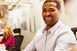 Smiling man sitting behind his desk holding a phone.