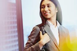 Business woman carrying her bag smiling, city in the background.