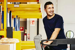 Smiling man standing on a forklift.