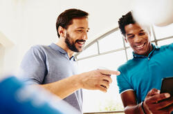 Two smiling colleagues (men) looking at a phone.