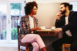 Woman and man sitting at a table with coffee. Having a conversation. Smiling.