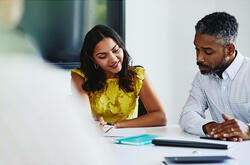 Man and woman sitting down, both looking at paperwork.