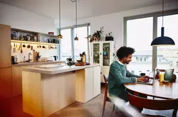Smiling male sitting at his dining table working on his laptop. Kitchen in the background.
