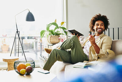 Smiling man sitting on a couch holding a notebook and a pen.