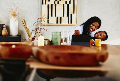 Smiling woman with kid on her lap sitting at a the kitchen table with tablet.