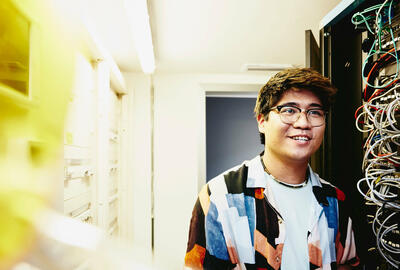 Smiling man holding a laptop standing in a servers room.