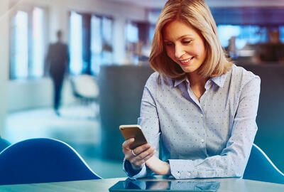 Woman in a blue shirt looking at her phone, sitting in an office. Primary color: blue.