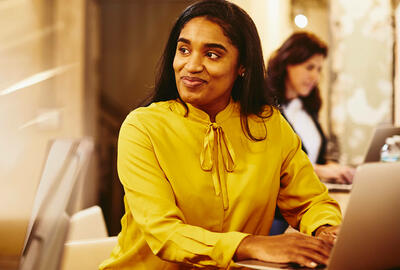 woman wearing a yellow shirt working on a laptop