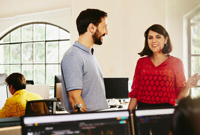 Two colleagues man and woman having a chat standing between desks.