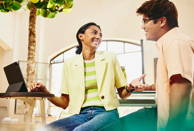 Man and woman sitting at table having a chat, while woman working on a tablet.