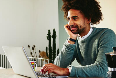 Man leaning against the counter top, while working on laptop.